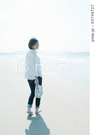 砂浜を靴を持って裸足で歩く女性 63749727