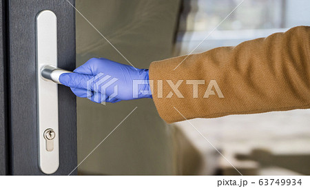 A hand in a protective glove on the handle of the front door. Protections in the midst of an epidemic A hand in a protective glove on the handle of the front door. Protections in the midst of an epidemic 63749934