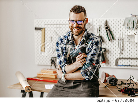 Cheerful craftsman with drill looking at camera Cheerful craftsman with drill looking at camera 63753084