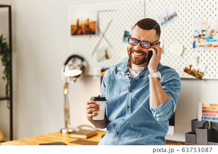 Cheerful man with cup of coffee talking on phone Cheerful man with cup of coffee talking on phone 63753087