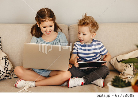 Cheerful children with gadgets sitting on sofa. Cheerful children with gadgets sitting on sofa. 63753088