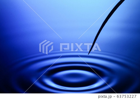 水面に植物の水滴が落ちて波紋が広がる様子の写真素材