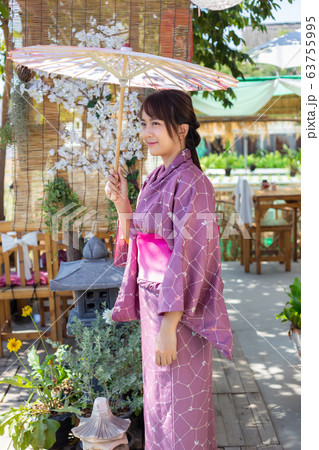 The girl is wearing a pink traditional yukata, which is the national dress of Japan and Hold an umbrella The girl is wearing a pink traditional yukata, which is the national dress of Japan and Hold an umbrella 63755995