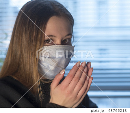 Virus spreading. Young woman looking at the camera sneezing or coughing in a protective medical face mask Virus spreading. Young woman looking at the camera sneezing or coughing in a protective medical face mask 63766218