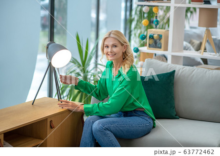 Blonde woman in a green blouse sitting near the lamp 63772462