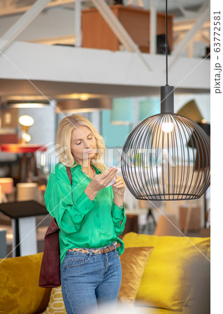 Blonde woman in a green blouse standing near the cage with a bird 63772581
