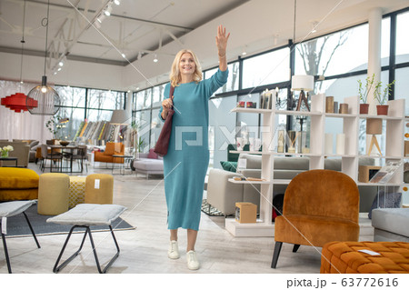 Blonde woman in a blue dress standing and waving her hand Blonde woman in a blue dress standing and waving her hand 63772616