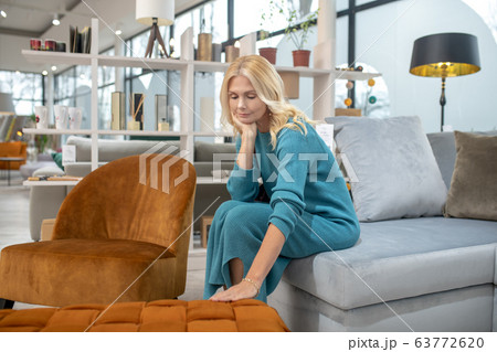 Blonde woman in a blue dress touching the sofa Blonde woman in a blue dress touching the sofa 63772620