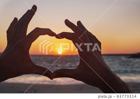 Male hands in the shape of a heart on sunset near the ocean Male hands in the shape of a heart on sunset near the ocean 63773314