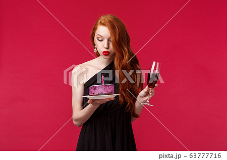 Silly good-looking redhead woman in slim black dress feel drunk after having few glasses champagne, hold glass and b-day cake, blowing out candle and making with during birthday party Silly good-looking redhead woman in slim black dress feel drunk after having few glasses champagne, hold glass and b-day cake, blowing out candle and making with during birthday party 63777716