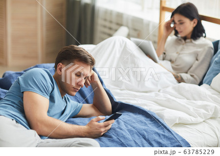 Distanced Couple Using Smartphones in Bed Distanced Couple Using Smartphones in Bed 63785229