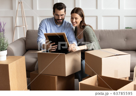 Happy young family couple unpacking belongings, looking at family photo. 63785595