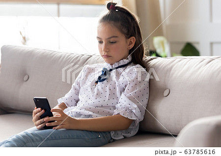Serious little schoolgirl using smartphone mobile apps alone at home. 63785616
