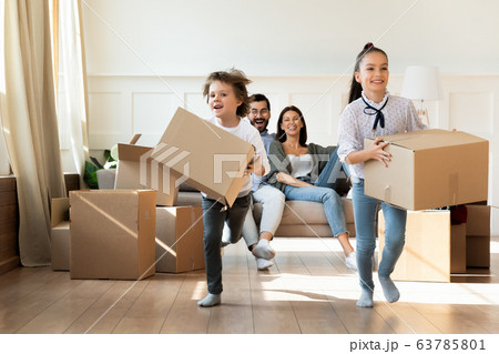 Happy young family couple watching little children running with boxes. Happy young family couple watching little children running with boxes. 63785801
