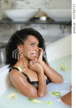 Relaxed beautiful black girl lying in milk bath and wearing swimsuit. 63786721