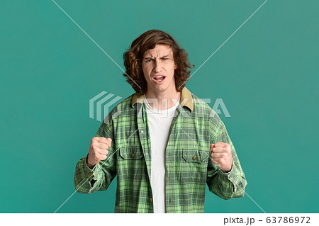 Conflict concept. Stressed millennial guy clenching fists on color background 63786972