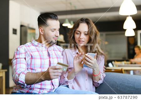 Young nice woman and man using smartphone and debit card at cafe. Young nice woman and man using smartphone and debit card at cafe. 63787290