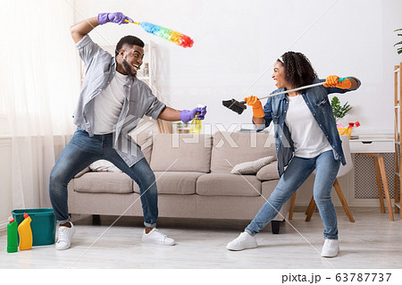 Cheerful Black Couple Fooling While Tidying Up Their Flat, Playfully Fighting 63787737