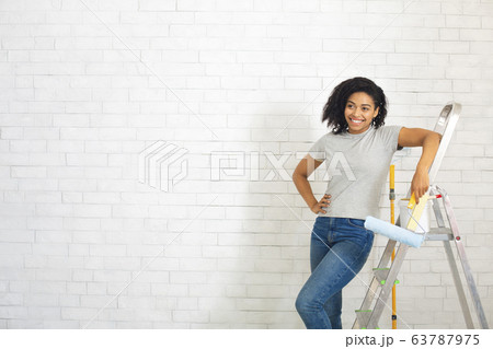 Woman beside stepladder with roller in hand on white brick wall background 63787975