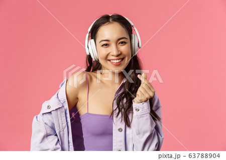 Close-up portrait of attractive happy young modern asian girl, listening music in headphones, show korean heart sign, enjoying favorite music or podcast, bought earphones with discount 63788904