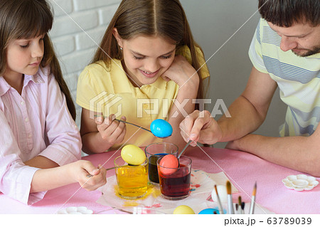 Daddy paint eggs in glasses with colorful dyes. 63789039