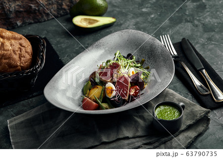 Nicoise salad with tuna on a gray plate, on a serving table. A beautiful dish from the chef, food photo, gray background, copy space, traditional French cuisine. Nicoise salad with tuna on a gray plate, on a serving table. A beautiful dish from the chef, food photo, gray background, copy space, traditional French cuisine. 63790735