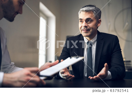 Smiling male colleagues are discussing their plans indoors Smiling male colleagues are discussing their plans indoors 63792541