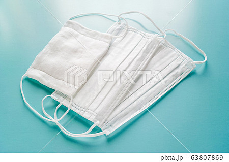 青いテーブルの上に置いた二枚の白い不織布マスクと一枚のガーゼマスク 63807869