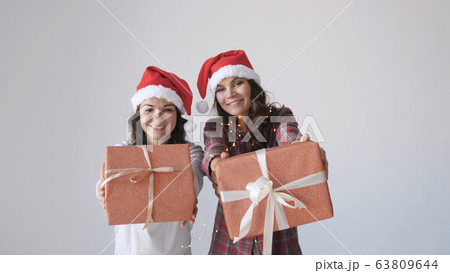 Young happy women in Christmas cap gives a gift box on a white background. Holidays packaging, wrapping. 63809644