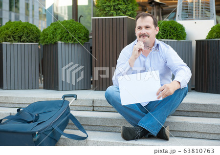 Sad man sitting on the steps with a suitcase Empty sign 63810763