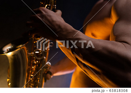 Muscular man naked torso playing on saxophone with smoked colorful background  63818308