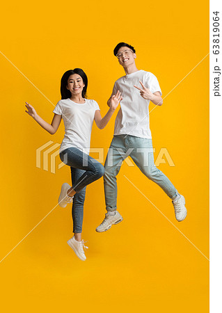 Excited asian couple of hipsters having fun over yellow 63819064