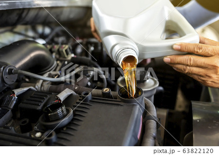 Car mechanic replacing and pouring fresh oil into engine at maintenance repair service station. Car mechanic replacing and pouring fresh oil into engine at maintenance repair service station. 63822120