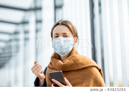 Woman with face mask and smart phone during an epidemic outdoors 63823283