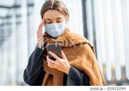 Woman with face mask and smart phone during an epidemic outdoors 63823289