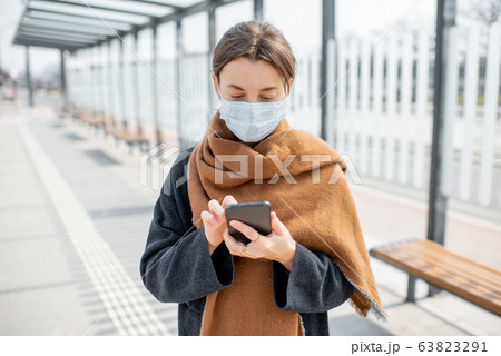 Woman with face mask and smart phone during an epidemic outdoors 63823291