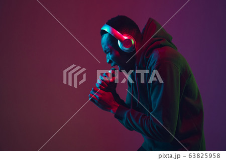African-american man's portrait with headphones isolated on gradient studio background in neon light African-american man's portrait with headphones isolated on gradient studio background in neon light 63825958