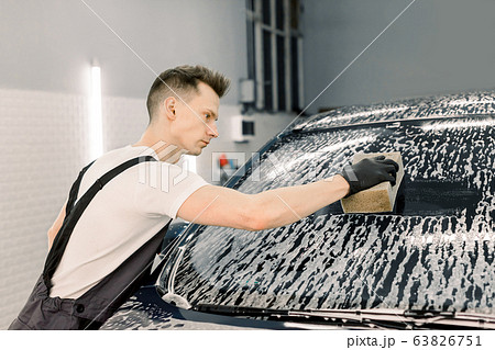 Car wash and clean with shampoo and sponge. Young handsome man worker washing soapy car windshield with sponge on a car wash. 63826751