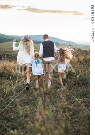 Back view photo of cheerful family in stylish fashionable clothes, parents and children, enjoying and running together in the mountains. Family in countryside, outdoors. Back view photo of cheerful family in stylish fashionable clothes, parents and children, enjoying and running together in the mountains. Family in countryside, outdoors. 63826892