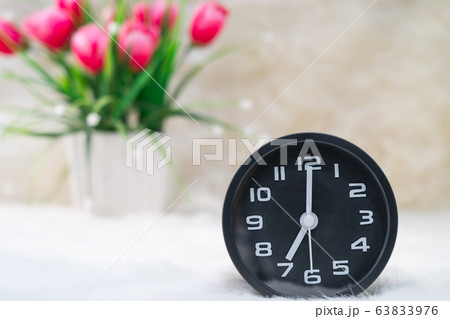 Black alarm clock and flower in vase on table 63833976