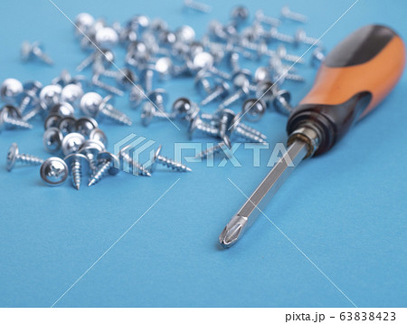 Metal screwdriver and many screws near. Soft focus 63838423