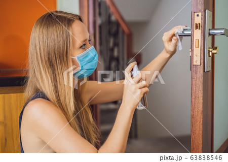 Woman hand is applying sanitizer on the door handle. Cleaning door handle with alcohol spray for 63838546