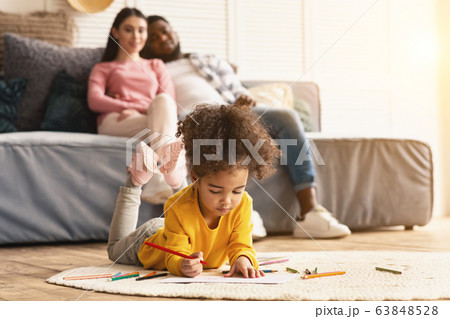 Child draws on the floor, parents sitting on couch Child draws on the floor, parents sitting on couch 63848528