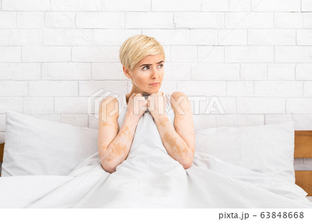Depressed woman in bed looking aside and covering by blanket 63848668