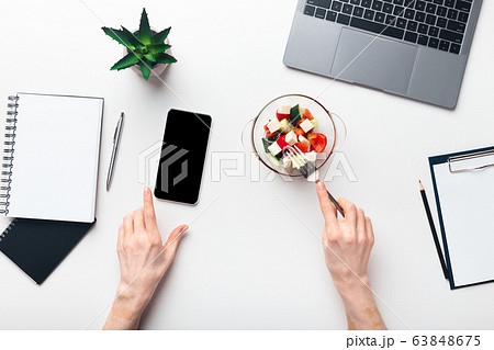 Woman eating fresh salad and looking at cellphone Woman eating fresh salad and looking at cellphone 63848675