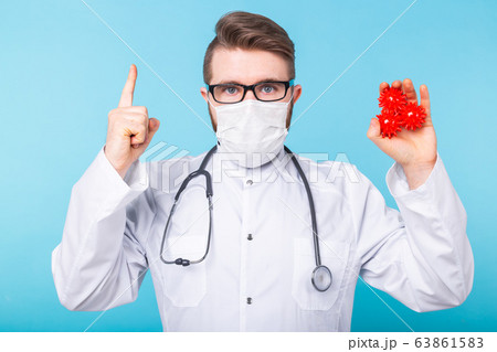 Covid-19, Vaccine development and medicine concept - Doctor in flu mask and protective gloves holding a model of coronavirus. Covid-19, Vaccine development and medicine concept - Doctor in flu mask and protective gloves holding a model of coronavirus. 63861583