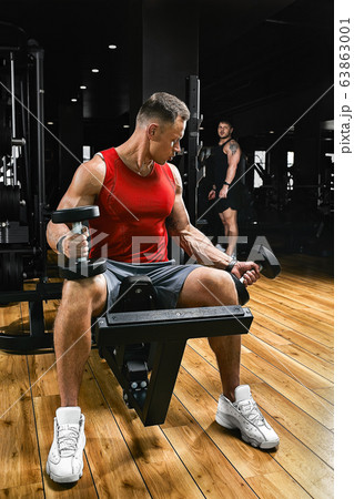 A shirtless muscular man is doing biceps exercises with dumbbell exercises as part of his bodybuilding workout. Fitness motivation, sports lifestyle, health, athletic body, body positive. Film grain 63863001