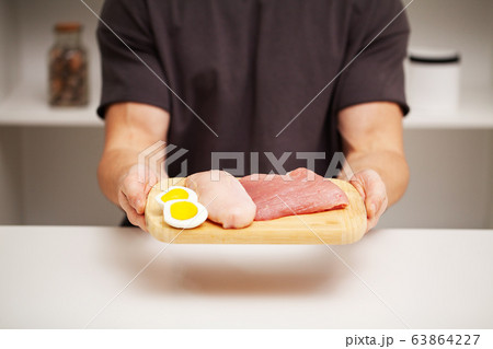 Athletic man holding a board with meat for proper nutrition of the athlete Athletic man holding a board with meat for proper nutrition of the athlete 63864227