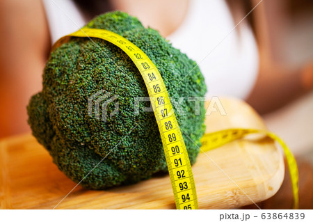 Closeup of woman holding broccoli with string tape to measure Closeup of woman holding broccoli with string tape to measure 63864839