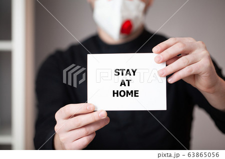 Man in a mask holds a sheet with the inscription stay at home 63865056